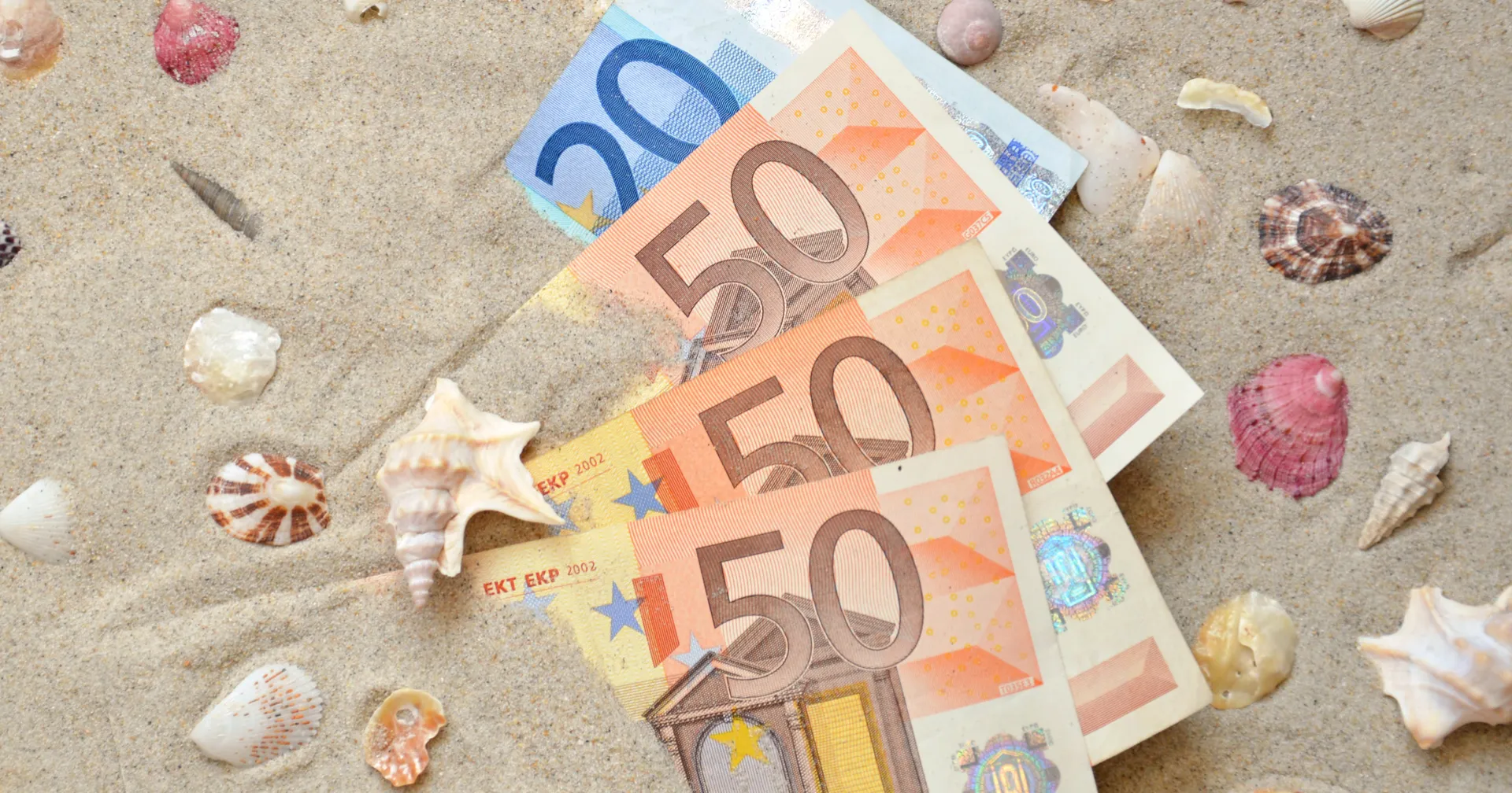 Meerdere briefjes geld op een strand met schelpen